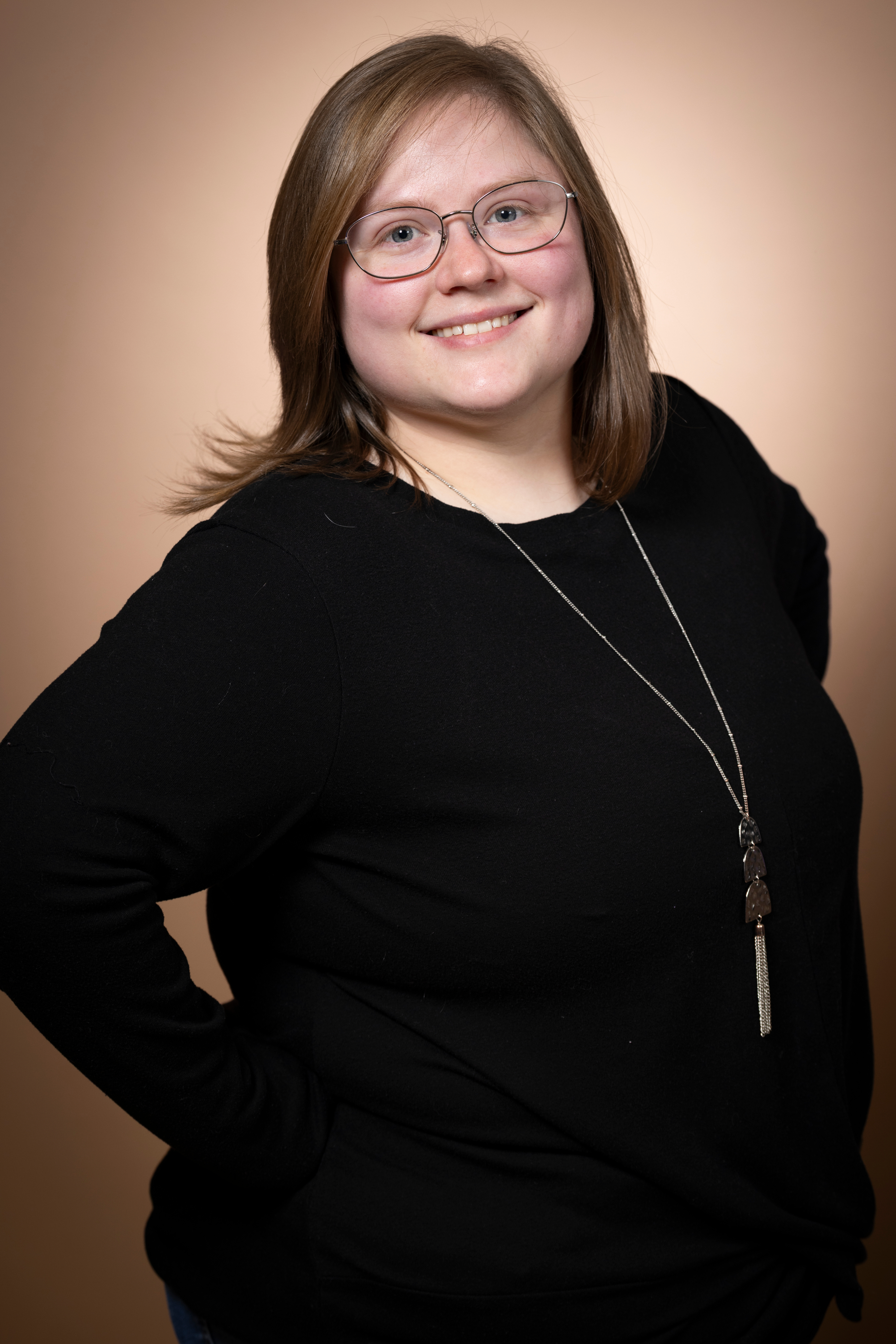 Jacquelyn's headshot. An image of a feminine person with short dirty blonde hair, wearing a white shirt that has a blue undershirt peeking through. They are looking towards the camera with a confident and warm closed mouth smile.
